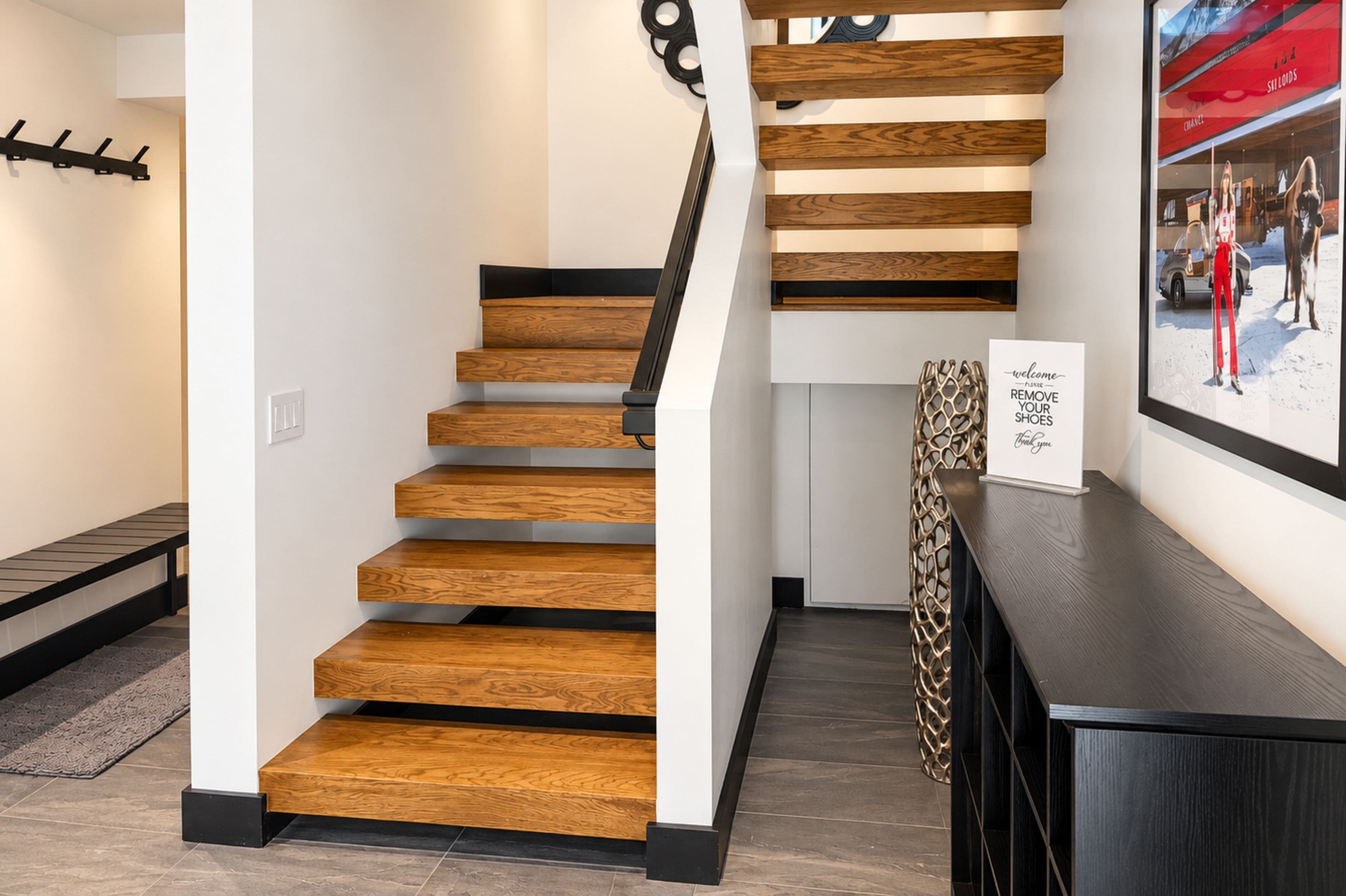A modern staircase with wooden steps and black handrails, leading to a landing with a framed welcome sign.