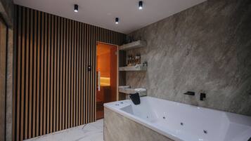 Un baño moderno con una bañera grande, pared con listones de madera y suelo de mármol.