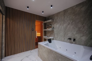 Un baño moderno con una bañera grande, pared con listones de madera y suelo de mármol.
