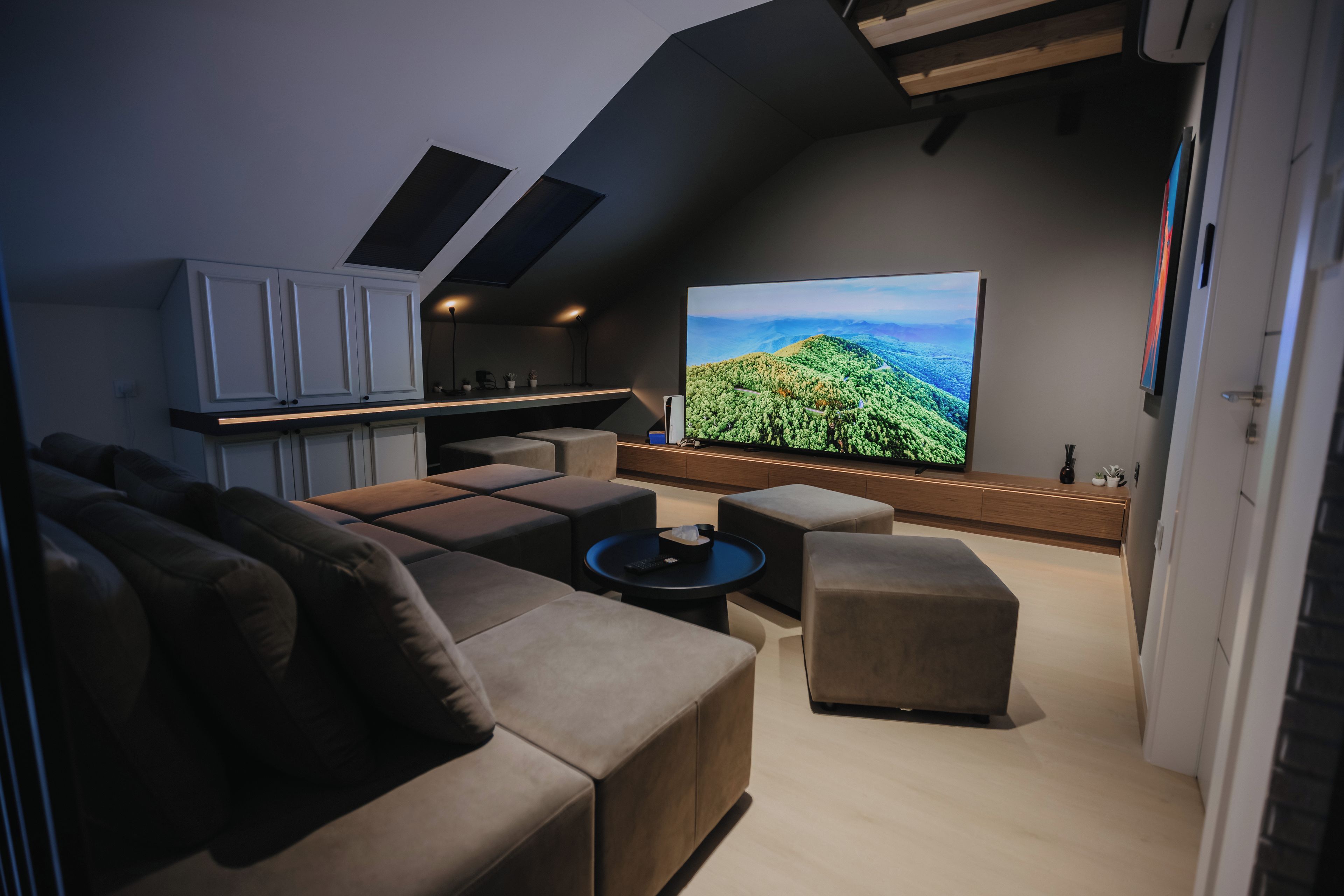 A modern living room with a large flat-screen TV, a sofa, a coffee table, and a kitchen area with cabinets.