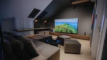 A modern living room with a large flat-screen TV, a sofa, a coffee table, and a kitchen area with cabinets.