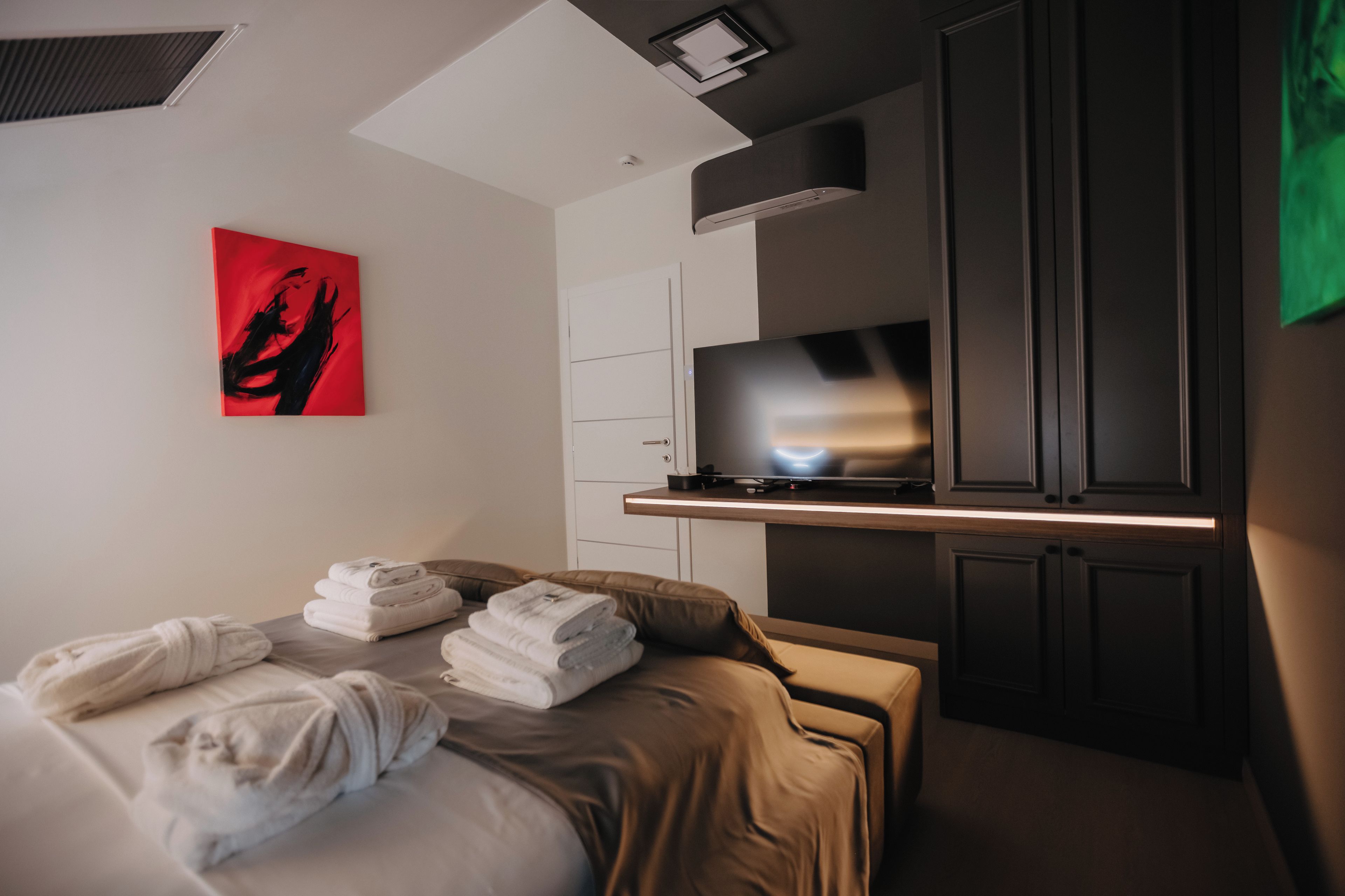 A hotel room with a bed, a flat-screen TV, a painting, and a cabinet.