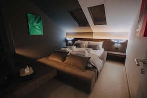 Una habitación de hotel compacta con cama, mesitas de noche, un pequeño sofá y un cuadro abstracto verde en la pared.