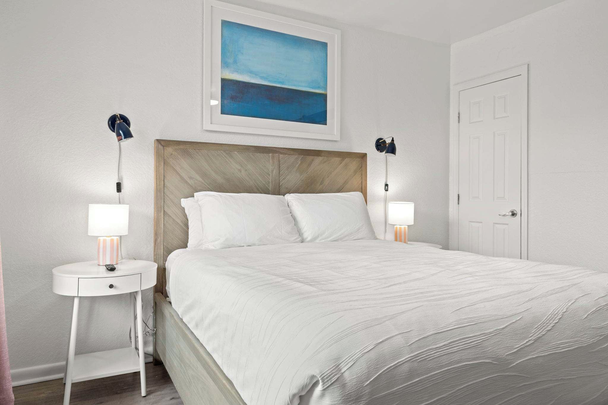 A neatly made bed with white linens in a room with white walls, a wooden headboard, and two bedside lamps.