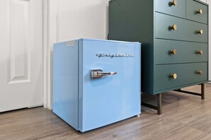 Ein blauer, kleiner Kühlschrank mit Metallgriff und dem Schriftzug 'Frigidaire', platziert neben einem grünen Schrank mit mehreren Schubladen.