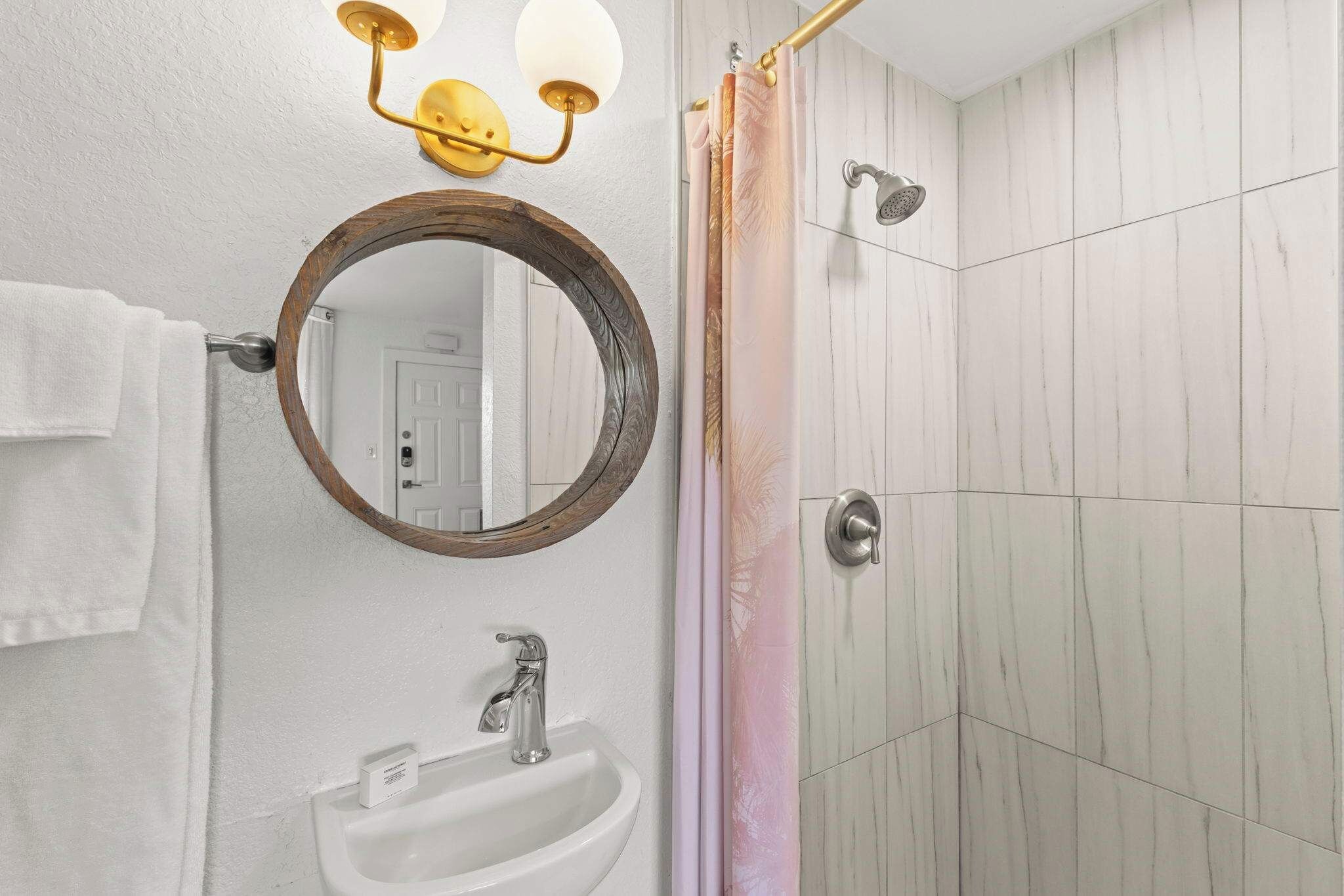 A bathroom with a round mirror, a sink, a shower with a glass door, and a towel hanging on the wall.