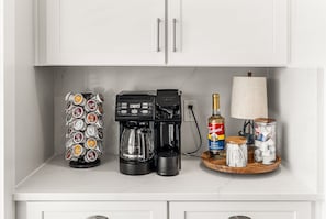 Eine Küchenarbeitsplatte mit einer Kaffeemaschine, einem Kaffee-Pods-Halter, einer Flasche Torani-Sirup sowie Zuckerdosen und Kaffee-Pods.
