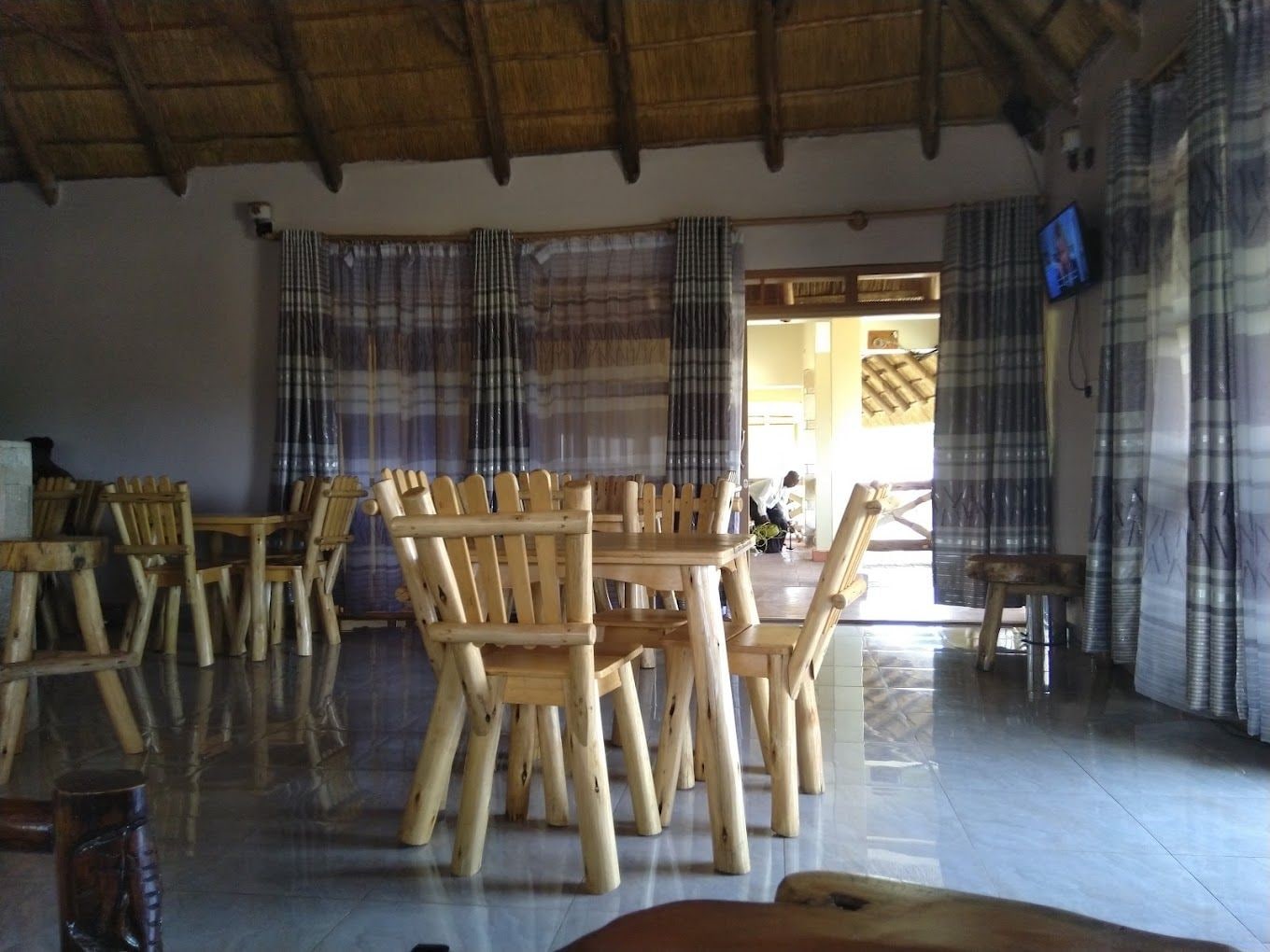A spacious room with a high ceiling and a thatched roof. There are wooden chairs and a table in the center, and a television mounted on the wall.