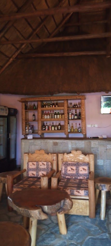 A rustic interior with wooden furniture, a bar area with shelves of bottles, and a stone wall.
