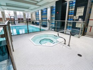 An indoor swimming pool with a hot tub, glass railings, and a tiled floor. - Chic Mississauga Condo with Pool, Gym & City Views (Mississauga)