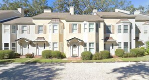 A row of townhouses with a symmetrical facade, evenly spaced windows, and a gravel driveway. - Summer Special – Condo Steps to Pier & Shops (St Simons Island)
