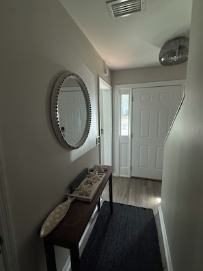 A hallway with a wooden bench, a decorative mirror, and a door leading to another room. - Summer Special – Condo Steps to Pier & Shops (St Simons Island)