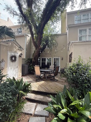 A patio with a table and chairs, surrounded by plants and a large tree. - Summer Special – Condo Steps to Pier & Shops (St Simons Island)