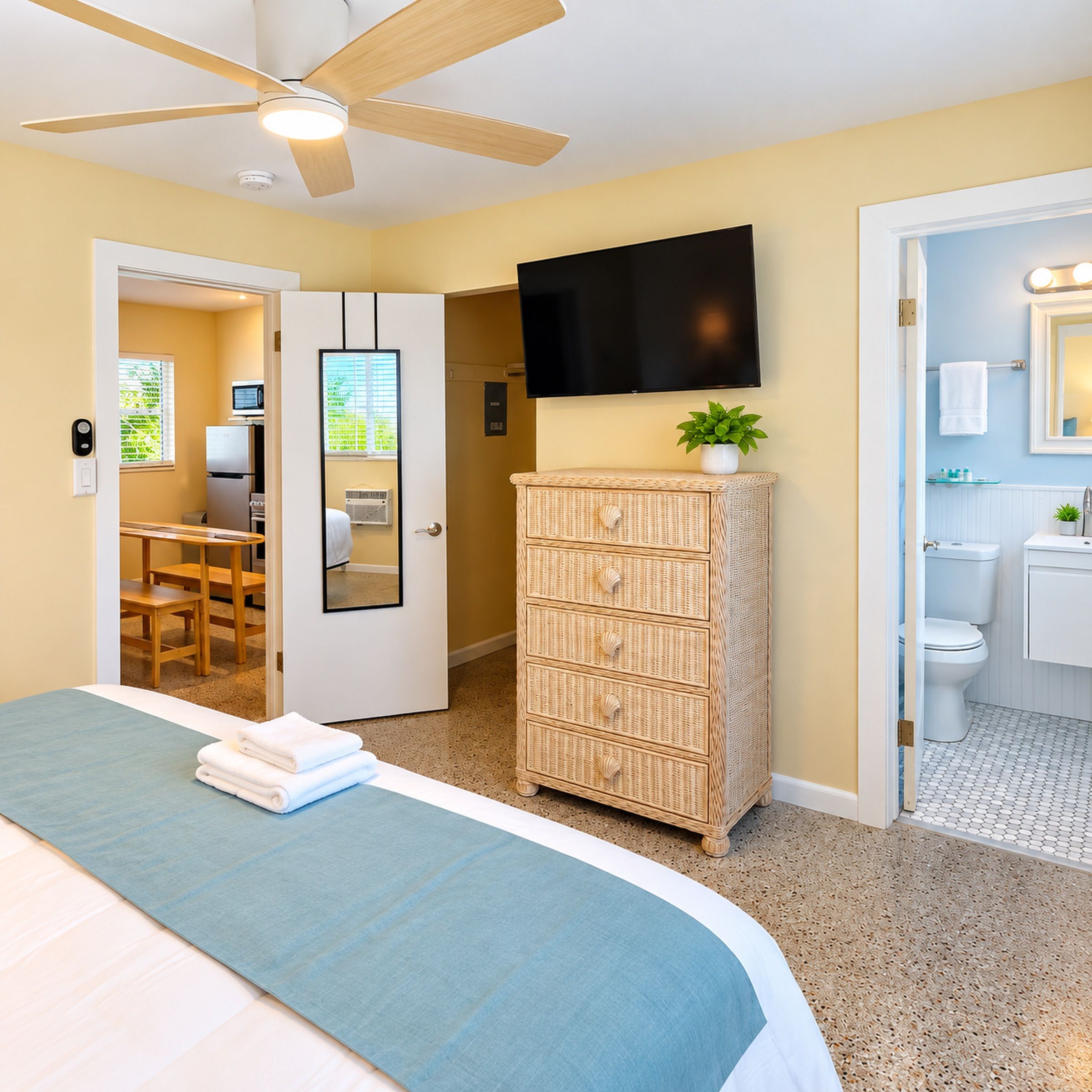 A hotel room with a bed, a television mounted on the wall, a wicker dresser, and a bathroom visible through an open door.
