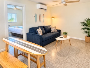 A modern living room with a sofa, a coffee table, a surfboard, and a ceiling fan. - Sunny Beach Inn - Ebb Tide Inn (Treasure Island)