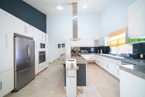 A modern kitchen with stainless steel appliances, white cabinetry, and a central island. - Private Villa Pool and Tennis Court 7BR (Cancún)