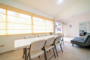 A room with a long table and chairs, a sofa, and a window with blinds. - Private Villa Pool and Tennis Court 7BR (Cancún)