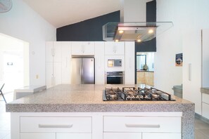 A modern kitchen with a granite countertop, stainless steel appliances, and white cabinetry. - Private Villa Pool and Tennis Court 7BR (Cancún)