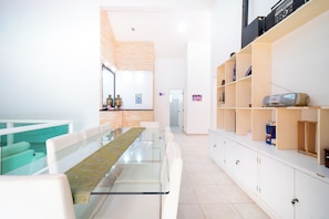 A modern interior with a glass dining table, white sofas, and a kitchen area with a brick wall. - Private Villa Pool and Tennis Court 7BR (Cancún)