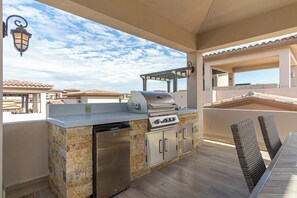 Eine Außenküche mit Grill und Kühlschrank, umgeben von Steinmauern und einer Holzterrasse.