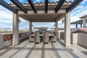 An outdoor patio with a dining table and chairs, a grill, and a view of the cityscape. - Luxury 2BR Condo at Quivira Los Cabos (Cabo San Lucas)