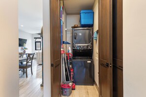 A narrow hallway with a refrigerator, a blue suitcase, and cleaning supplies. - Luxury 2BR Condo at Quivira Los Cabos (Cabo San Lucas)
