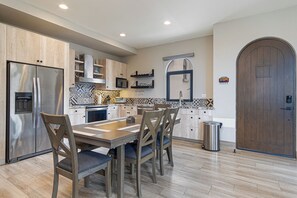 A modern kitchen with a stainless steel refrigerator, wooden cabinets, a dining table with four chairs, and a large wooden door. - Luxury 2BR Condo at Quivira Los Cabos (Cabo San Lucas)
