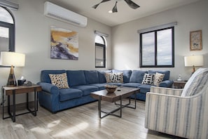 A living room with a blue sofa, patterned pillows, a coffee table, and a patterned armchair. - Luxury 2BR Condo at Quivira Los Cabos (Cabo San Lucas)