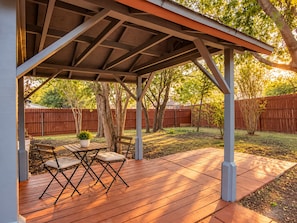 A covered patio with a wooden deck, a table, and two chairs. - Your Extended Stay Spot (Arlington)