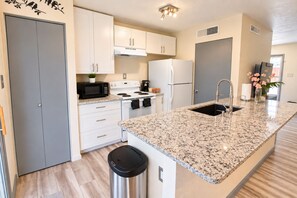 A modern kitchen with white cabinets, a granite countertop, a stainless steel sink, and a black trash bin. - Your Extended Stay Spot (Arlington)