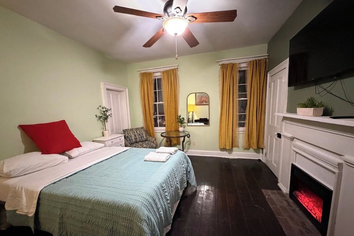 A bedroom with a bed, a chair, a fireplace, and a ceiling fan.