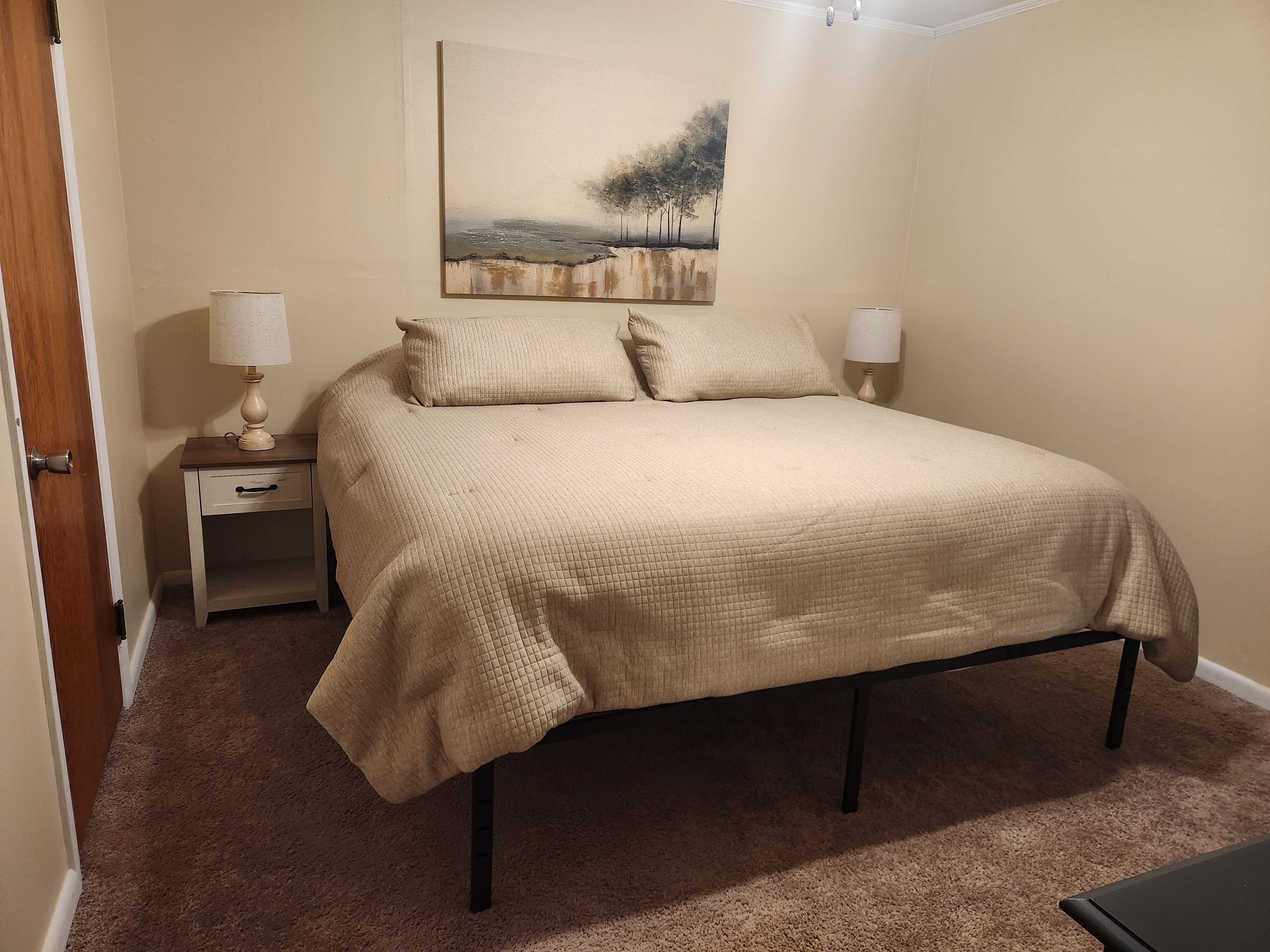 A bedroom with a bed, bedside tables, lamps, and a painting on the wall.