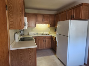A compact kitchen with wooden cabinets, a white refrigerator, a stove, and a sink.