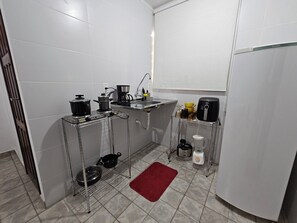 A compact kitchen with white tiles, a red rug, and various appliances on metal racks. - New Listing (João Pessoa)