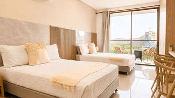 A hotel room with two beds, a large window with a view, a dining area with chairs, and an air conditioning unit.
