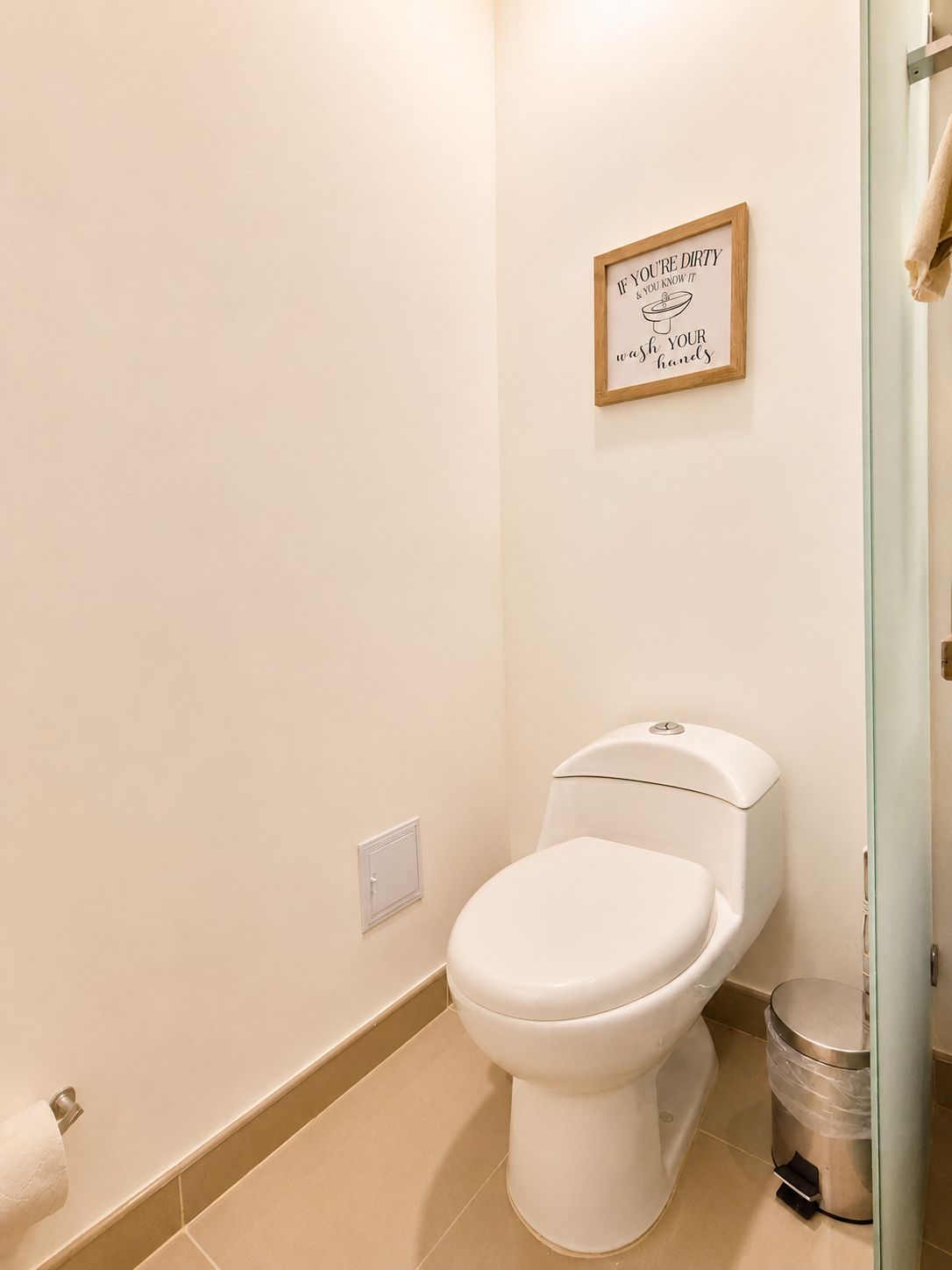 Ein Badezimmer mit Toilette, Mülleimer und einem gerahmten Schild an der Wand.