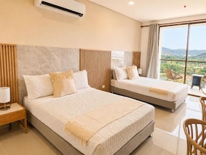 Habitació d'hotel amb dos llits, una finestra gran amb vistes i zona de menjador amb una cadira.
