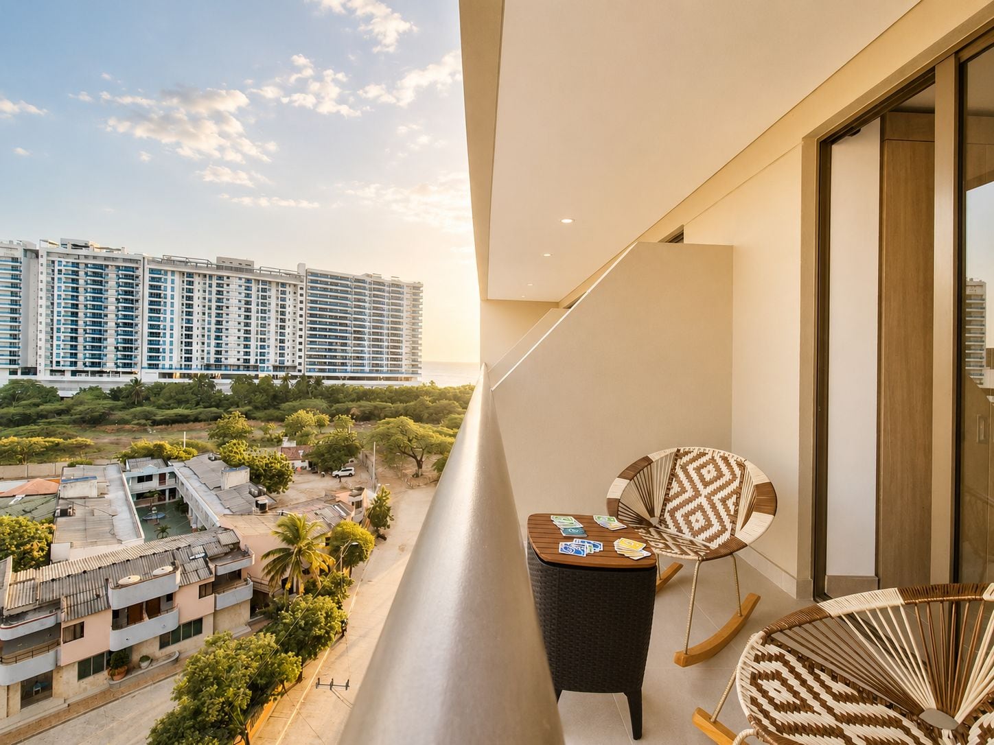 A balcony with a view of high-rise buildings, a small table with cards, and two wicker chairs.