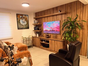 Una sala de estar con televisor, estanterías de madera, una planta en maceta, un sofá y un jarrón decorativo.