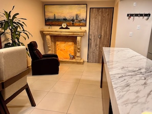 Een woonkamer met een open haard, een bank, een eettafel en een schilderij van een stadsbeeld.