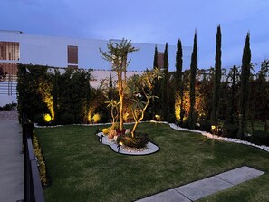 Un jardín ajardinado con diversas especies de árboles, un césped cuidado y un camino pavimentado.