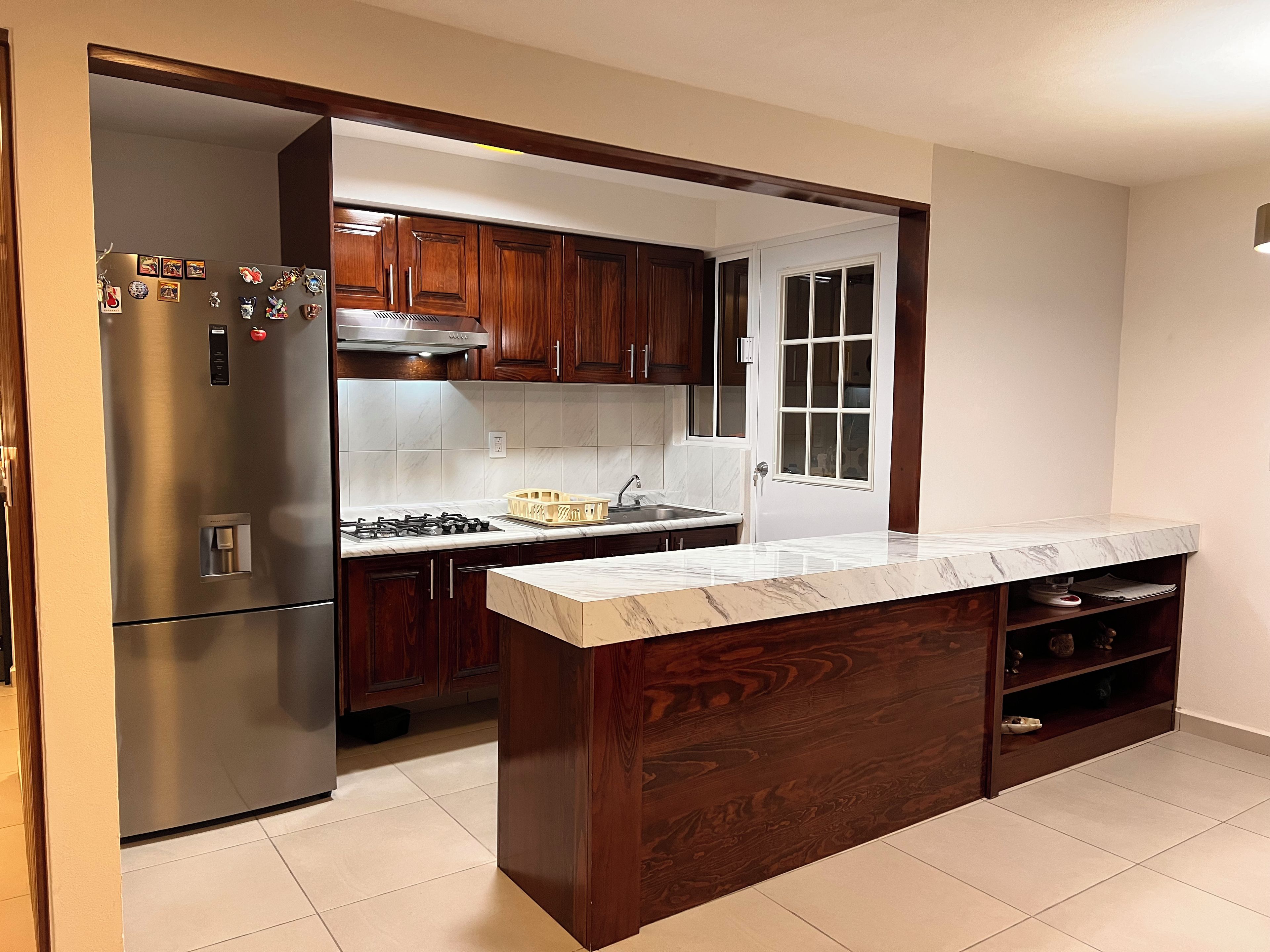 A kitchen with wooden cabinets, a stainless steel refrigerator, a marble countertop, and a built-in oven.