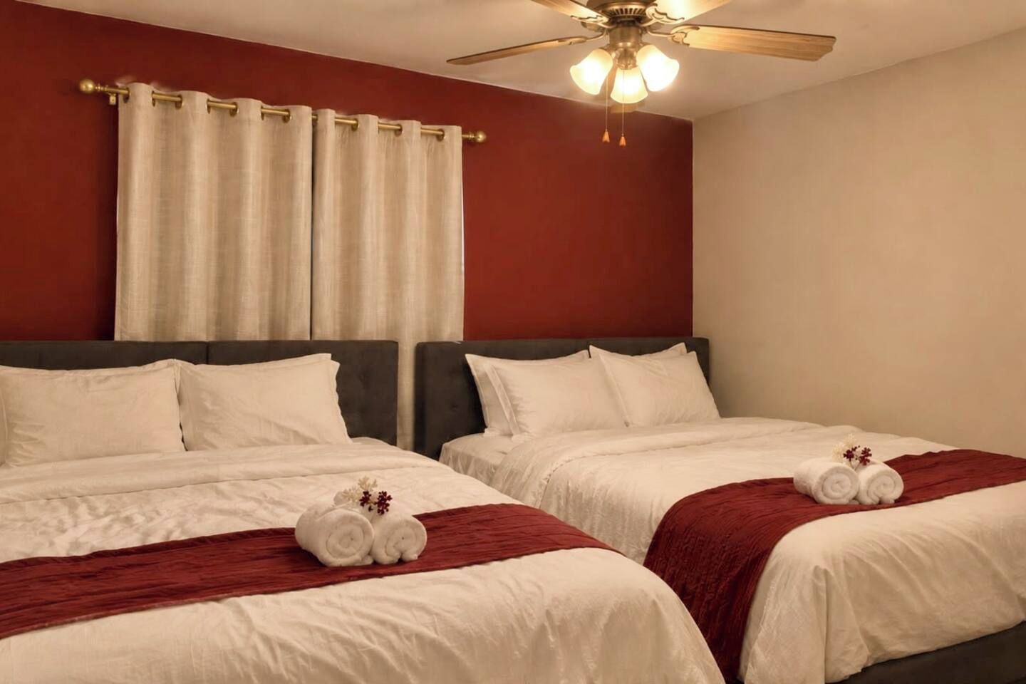 Een hotelkamer met twee bedden, een plafondventilator en een raam met gordijnen.