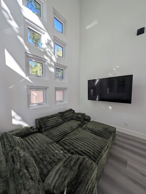 Una stanza con un letto, una TV a schermo piatto montata a parete e diverse finestre che lasciano entrare luce naturale.