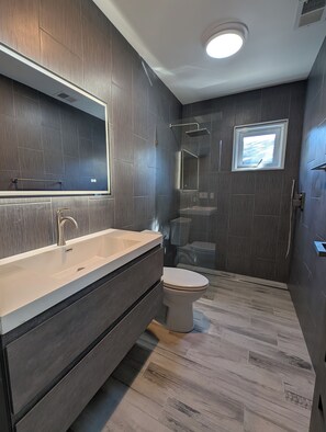 Un bagno moderno con uno specchio grande, un lavandino, un WC e una cabina doccia.