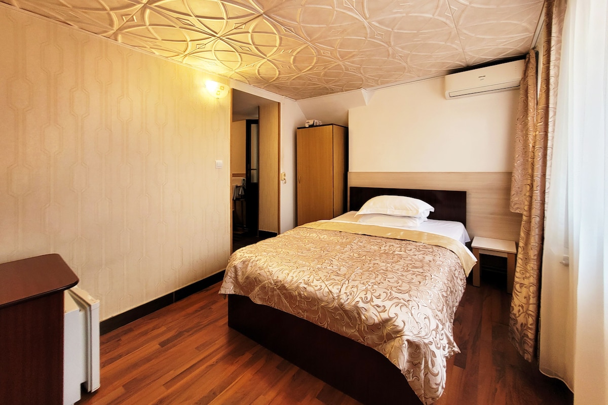 Une chambre d’hôtel comprenant un lit, une table de chevet, une armoire et un plafond orné d’un motif géométrique.