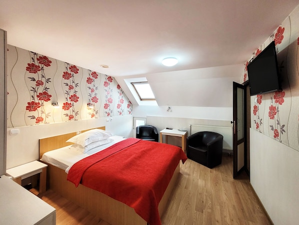 A bedroom with a bed, a desk, a chair, a television, and a skylight. - Pensiunea Dorobanti (Cluj-Napoca)