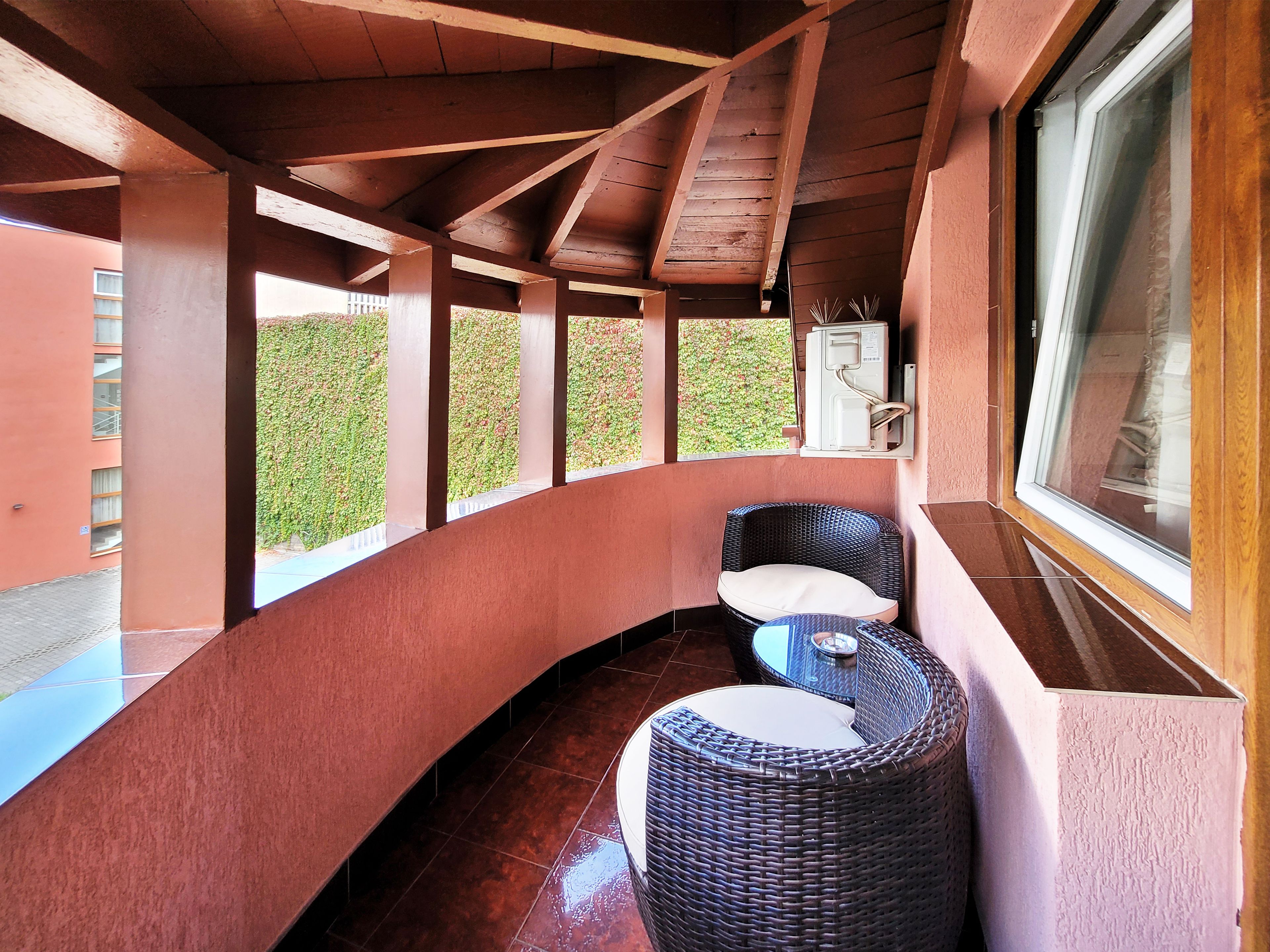 Un espacio de estar al aire libre techado con mobiliario de mimbre, una mesa de vidrio y vistas a la vegetación a través de las ventanas.