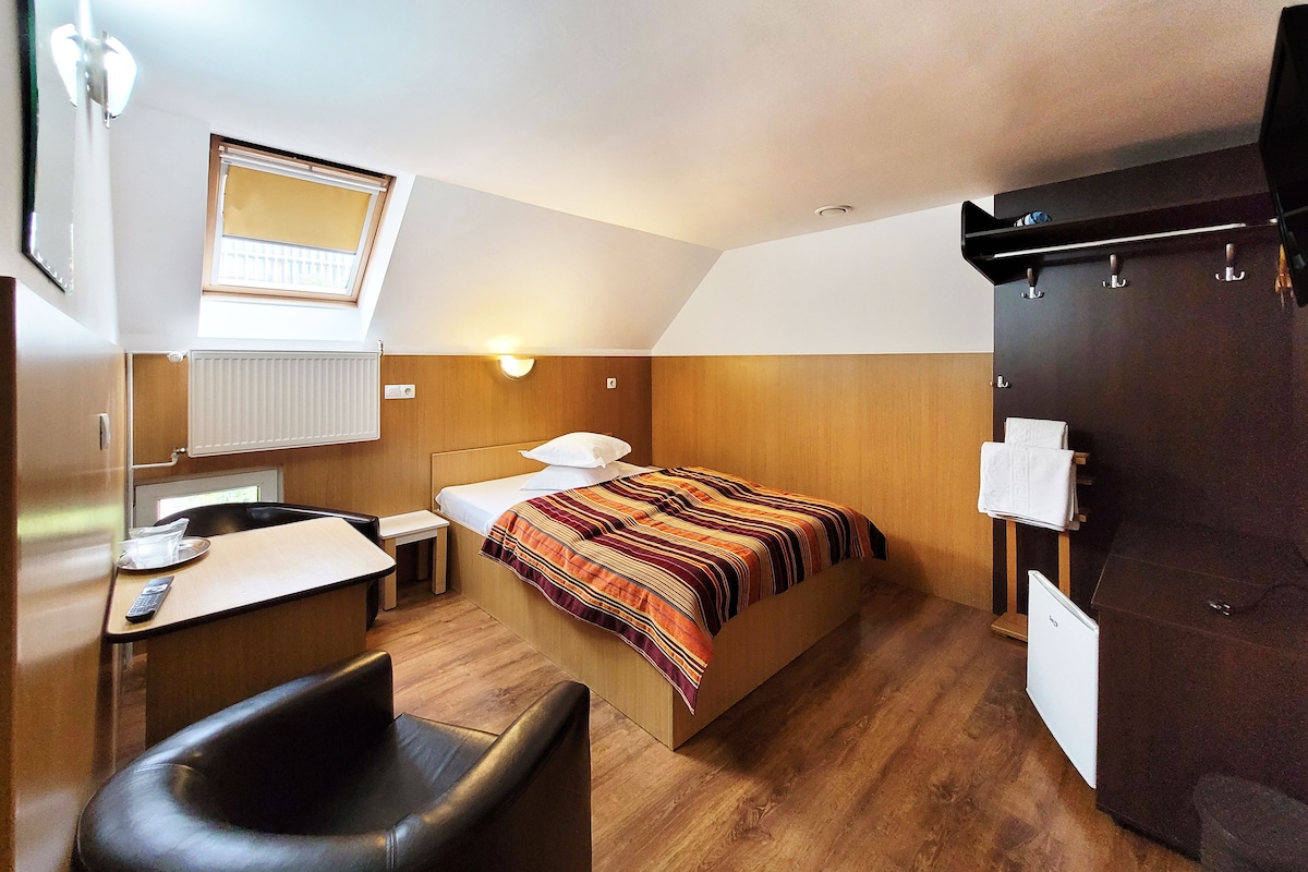 Une pièce de taille modeste comprenant un lit, un petit bureau, une chaise, un radiateur et une armoire.