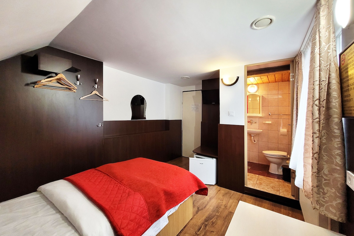 Une chambre à coucher avec un lit, une armoire, un miroir et une salle de bain visible à travers une porte ouverte.